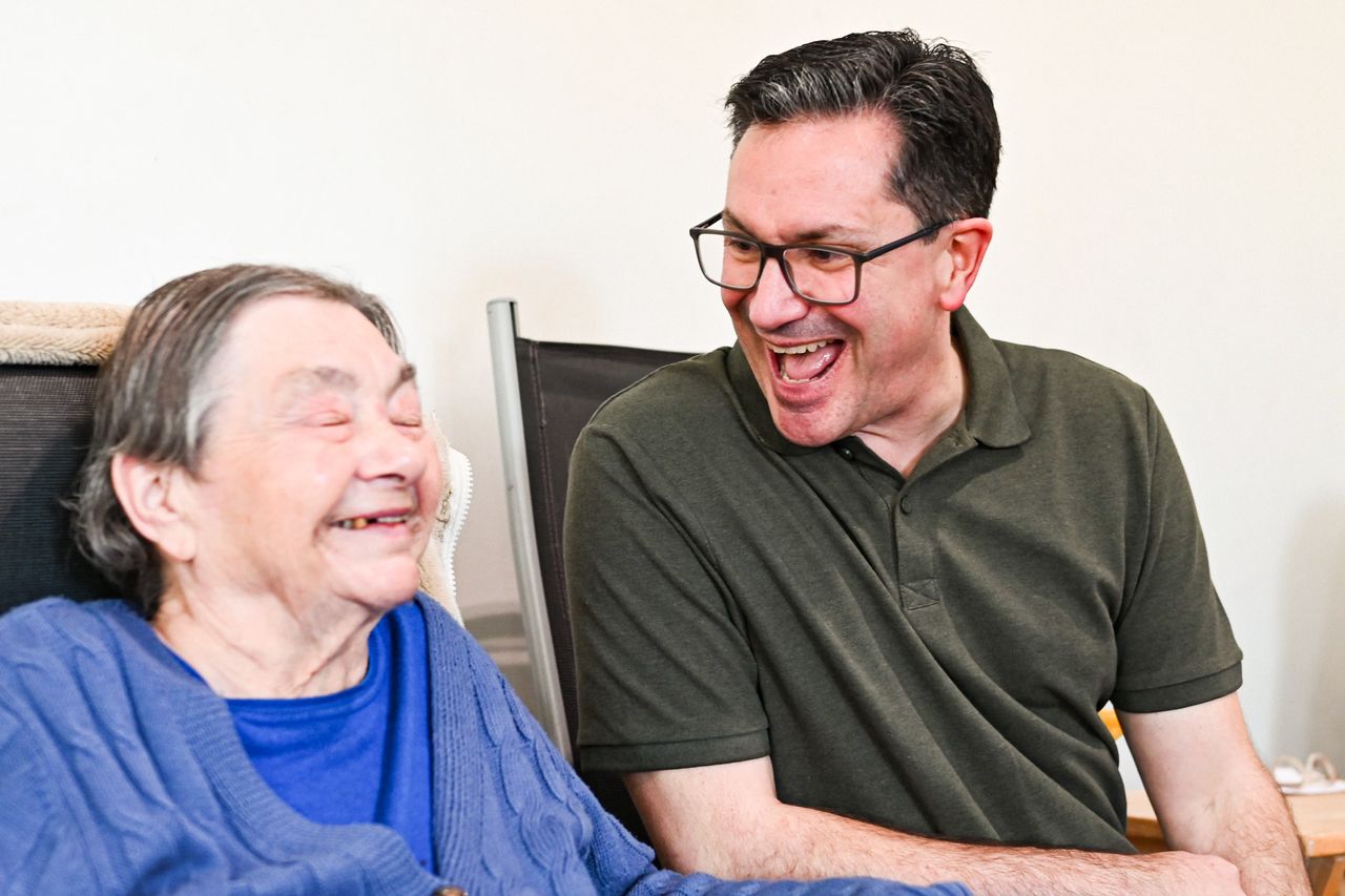 A man and an elderly woman share laughter indoors. Captured in Norwich, UK.